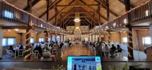 DJ in Maine setup at a barn wedding reception with string lights and guest seating
